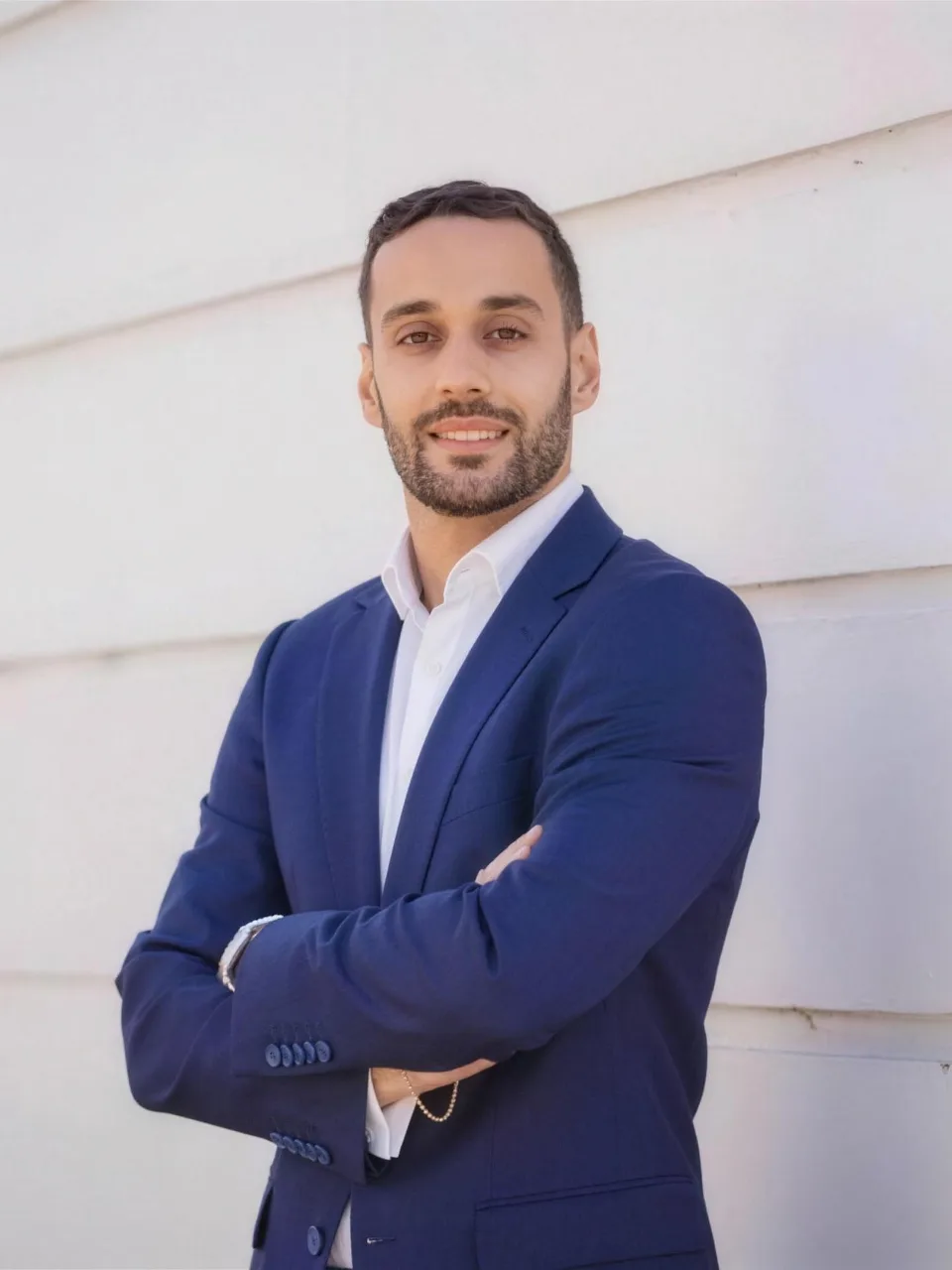 Omar El Deek, smiling, in a navy blazer with arms crossed